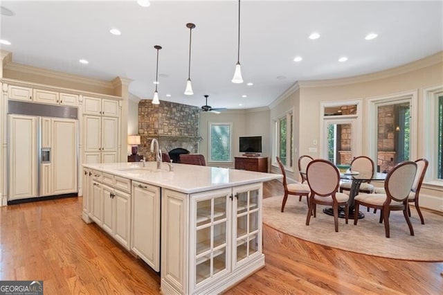 kitchen featuring hanging light fixtures, an island with sink, a fireplace, light wood-type flooring, and paneled fridge