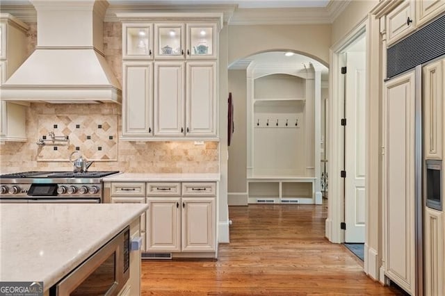 kitchen with premium range hood, tasteful backsplash, light hardwood / wood-style flooring, built in appliances, and crown molding