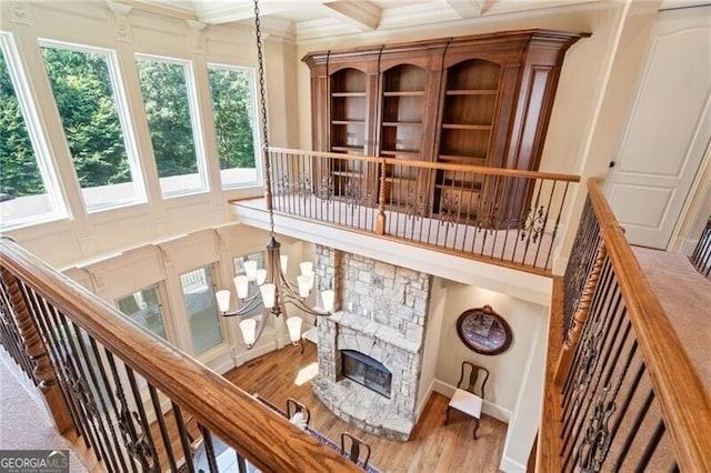 stairway featuring wood-type flooring, a notable chandelier, coffered ceiling, a stone fireplace, and ornamental molding