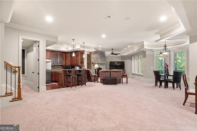 living room featuring a raised ceiling, a fireplace, ornamental molding, and light colored carpet