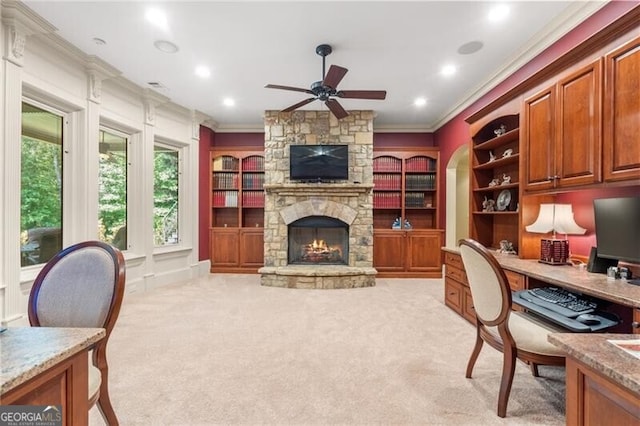 carpeted office featuring a stone fireplace, ceiling fan, and crown molding