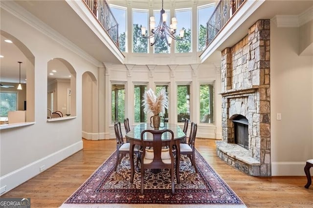 dining area with a stone fireplace, crown molding, hardwood / wood-style flooring, a notable chandelier, and a towering ceiling