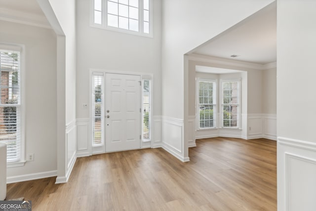 foyer with ornamental molding, light hardwood / wood-style floors, and a high ceiling