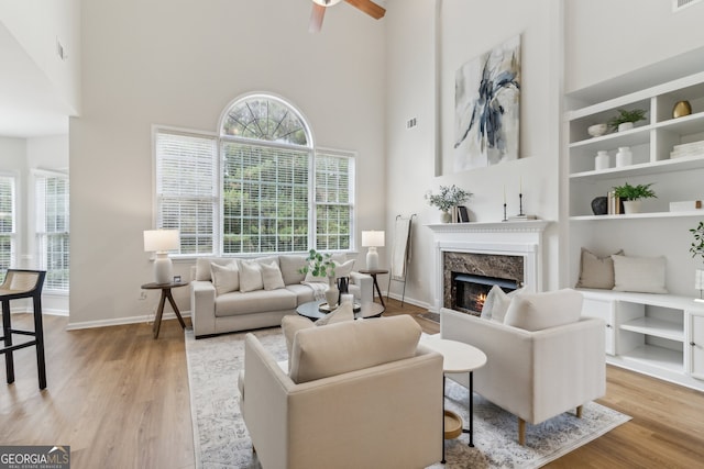 living room featuring light wood-type flooring, a high end fireplace, ceiling fan, and a high ceiling