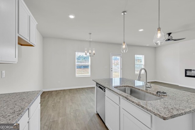 kitchen with white cabinets, ceiling fan with notable chandelier, a center island with sink, and sink