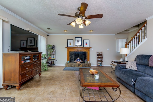 tiled living room with ceiling fan, a stone fireplace, a textured ceiling, and crown molding