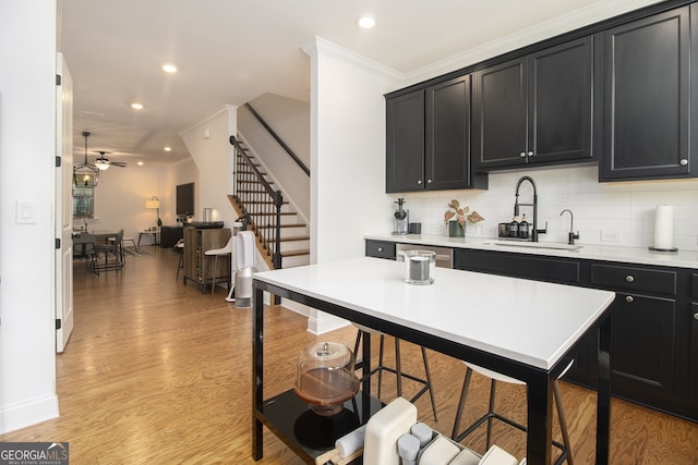 kitchen featuring a breakfast bar, ceiling fan, crown molding, sink, and light hardwood / wood-style floors