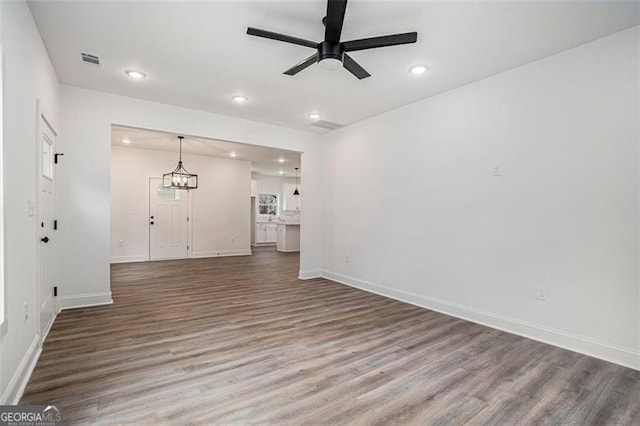 unfurnished living room featuring ceiling fan with notable chandelier and dark wood-type flooring