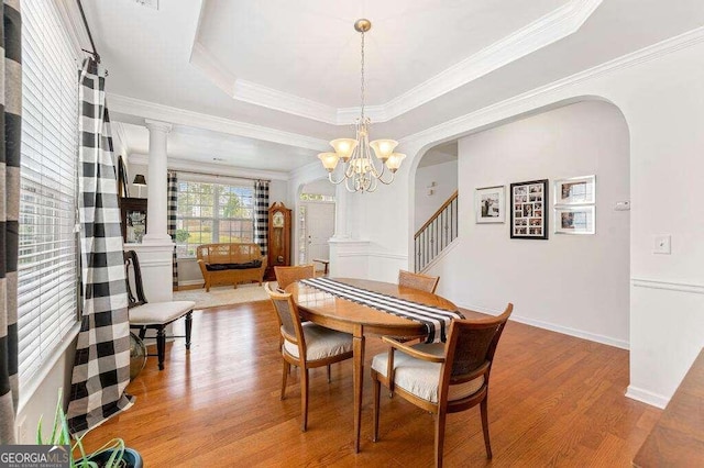 dining space featuring a tray ceiling, ornate columns, light hardwood / wood-style floors, and an inviting chandelier