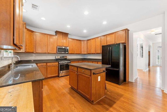 kitchen with appliances with stainless steel finishes, light wood-type flooring, dark stone counters, sink, and a kitchen island