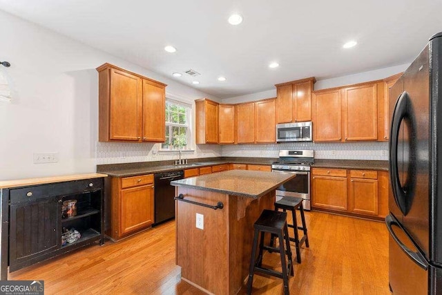 kitchen with a kitchen bar, a center island, black appliances, and light hardwood / wood-style flooring