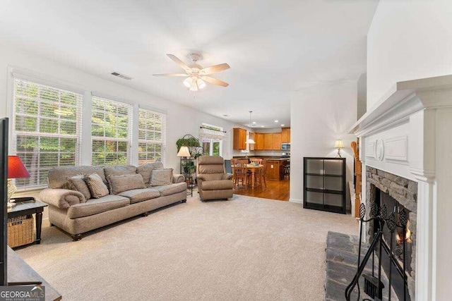 living room featuring ceiling fan, a fireplace, and light colored carpet