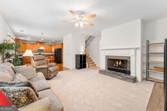 living room with light carpet, a stone fireplace, and ceiling fan