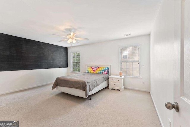 bedroom featuring ceiling fan, light colored carpet, and multiple windows