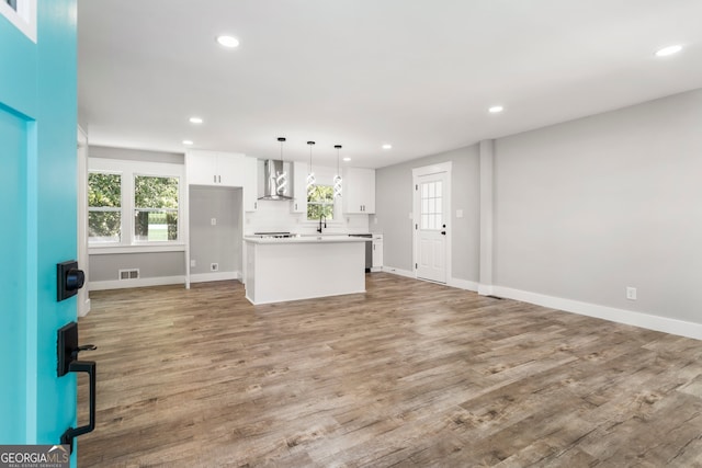 kitchen featuring a healthy amount of sunlight, wall chimney range hood, a kitchen island, hanging light fixtures, and white cabinetry