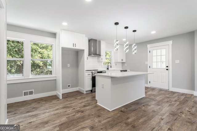 kitchen featuring wall chimney range hood, sink, white cabinetry, stainless steel appliances, and pendant lighting