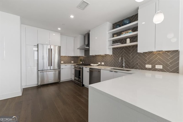 kitchen with wall chimney exhaust hood, dark wood-type flooring, pendant lighting, white cabinetry, and appliances with stainless steel finishes