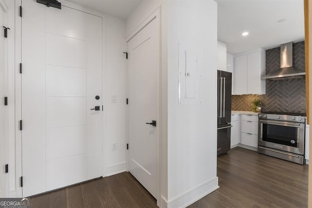 interior space with white cabinets, wall chimney range hood, stainless steel appliances, and dark hardwood / wood-style flooring