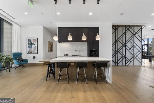 kitchen featuring sink, a kitchen bar, light hardwood / wood-style flooring, and pendant lighting