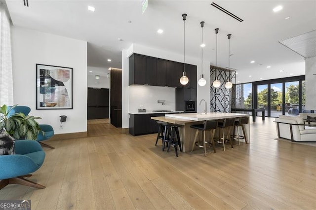 kitchen with a kitchen island with sink, sink, a breakfast bar, decorative light fixtures, and light hardwood / wood-style floors