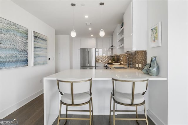 kitchen with kitchen peninsula, sink, pendant lighting, white cabinets, and stainless steel refrigerator