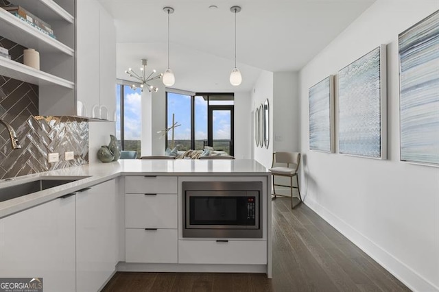 kitchen with stainless steel microwave, kitchen peninsula, pendant lighting, white cabinets, and tasteful backsplash