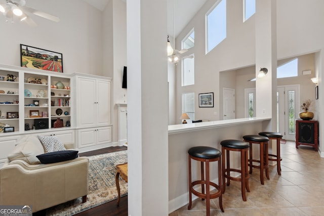 kitchen featuring high vaulted ceiling, white cabinetry, ceiling fan, and a breakfast bar area