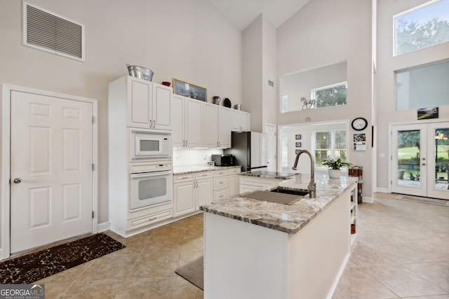 kitchen with white cabinets, light stone countertops, white appliances, and high vaulted ceiling