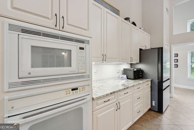 kitchen featuring light stone countertops, white appliances, white cabinetry, and light tile patterned floors