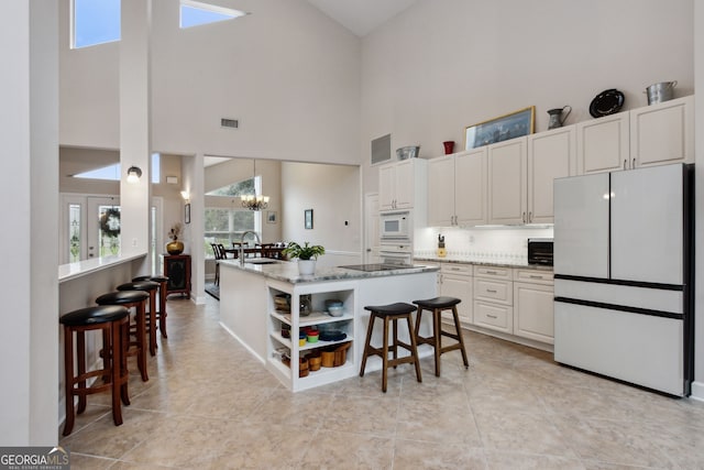 kitchen with a breakfast bar, a chandelier, white appliances, light stone countertops, and a high ceiling