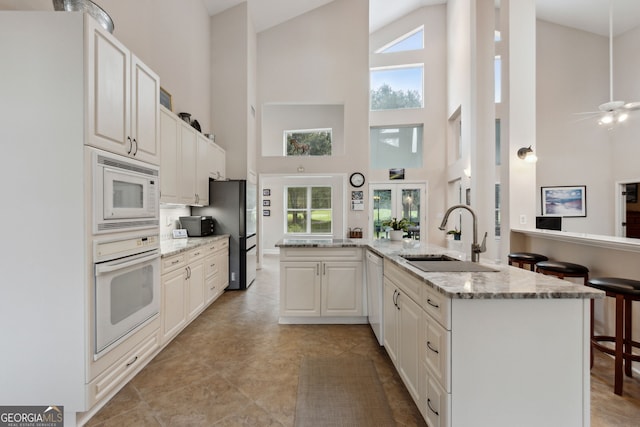 kitchen featuring high vaulted ceiling, white appliances, kitchen peninsula, and sink