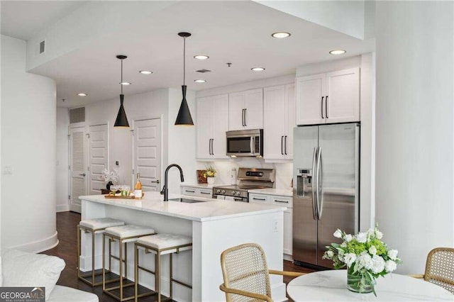 kitchen featuring white cabinets, sink, a kitchen island with sink, decorative light fixtures, and appliances with stainless steel finishes