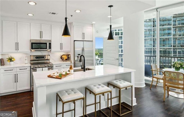 kitchen featuring appliances with stainless steel finishes, dark wood-type flooring, backsplash, decorative light fixtures, and a kitchen island with sink