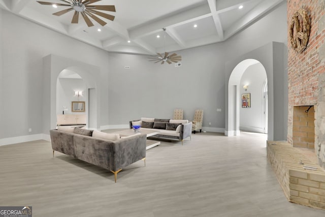 living room featuring beam ceiling, a fireplace, a high ceiling, and light hardwood / wood-style flooring