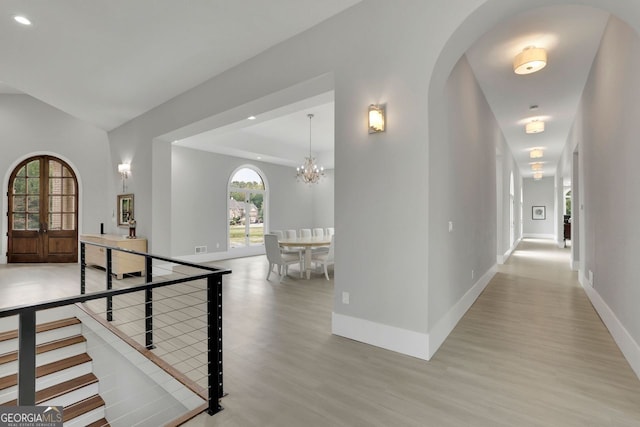 corridor featuring french doors, light wood-type flooring, and an inviting chandelier