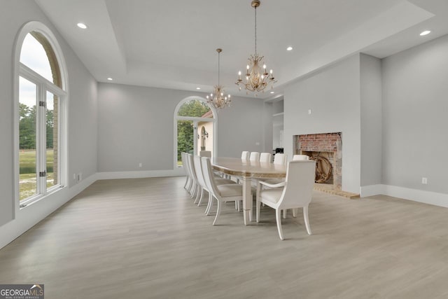 dining room with light wood-type flooring, a tray ceiling, a brick fireplace, and a notable chandelier