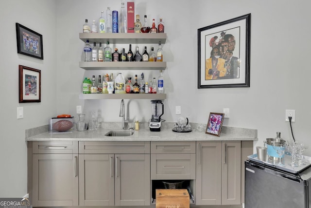 bar with gray cabinets, light stone counters, sink, and appliances with stainless steel finishes