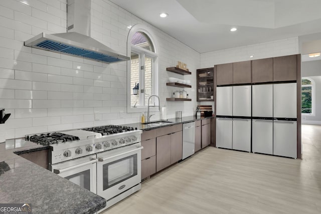 kitchen with dishwasher, sink, wall chimney exhaust hood, high end stainless steel range oven, and light wood-type flooring