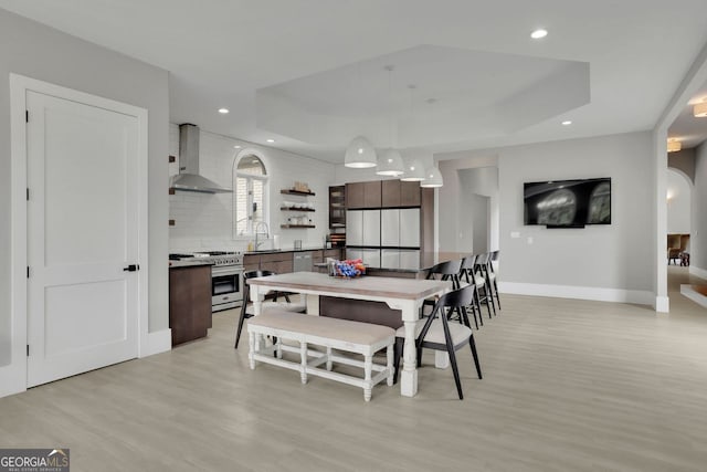 dining space featuring a raised ceiling, light wood-type flooring, and sink