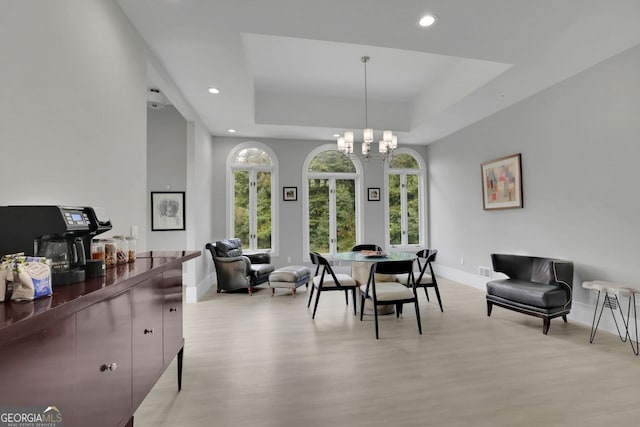 dining area featuring light hardwood / wood-style floors, a raised ceiling, and an inviting chandelier