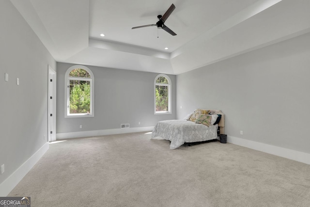 unfurnished bedroom with a raised ceiling, multiple windows, ceiling fan, and light carpet