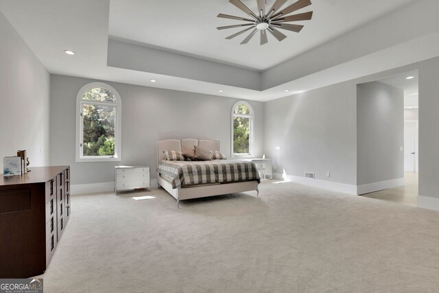 bedroom with a raised ceiling, ceiling fan, and light colored carpet