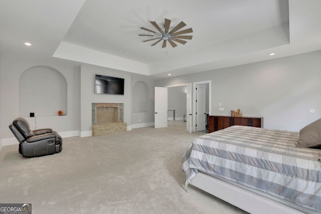 carpeted bedroom with ceiling fan, a raised ceiling, and a brick fireplace