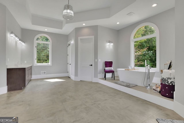 bathroom with a raised ceiling, a bathtub, vanity, and an inviting chandelier