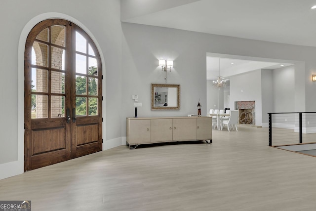 foyer entrance with light hardwood / wood-style floors, an inviting chandelier, french doors, and a brick fireplace