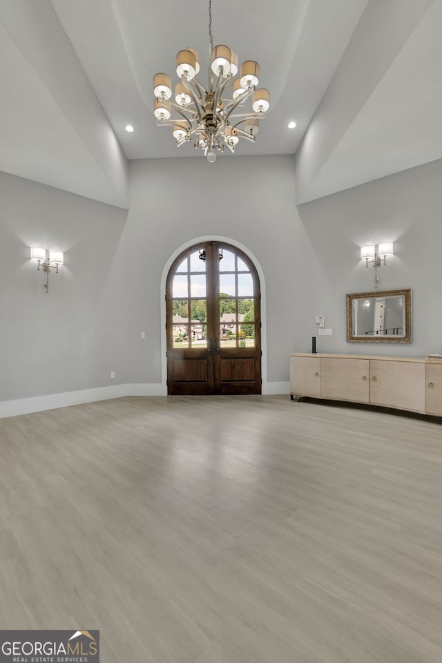 interior space featuring french doors, a towering ceiling, light hardwood / wood-style flooring, and a notable chandelier