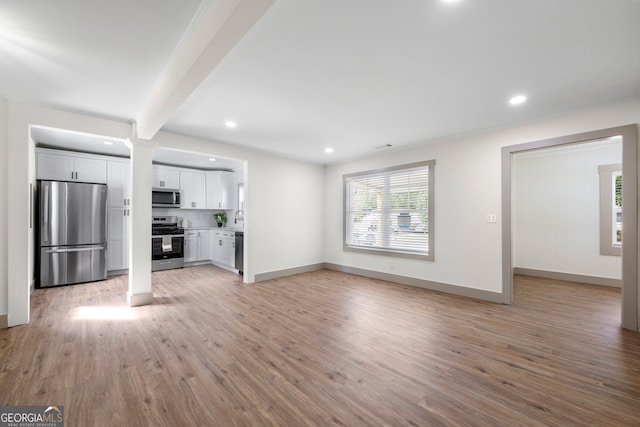 unfurnished living room featuring light wood-type flooring, beamed ceiling, and ornate columns