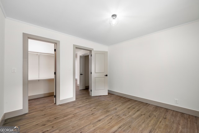 unfurnished bedroom featuring ornamental molding, a spacious closet, light hardwood / wood-style flooring, and a closet