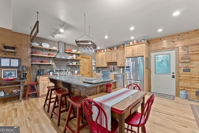 kitchen featuring a center island, a kitchen breakfast bar, wall chimney exhaust hood, light brown cabinetry, and appliances with stainless steel finishes