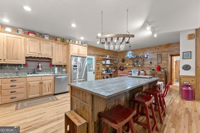 kitchen with light brown cabinetry, wood walls, a center island, and stainless steel appliances